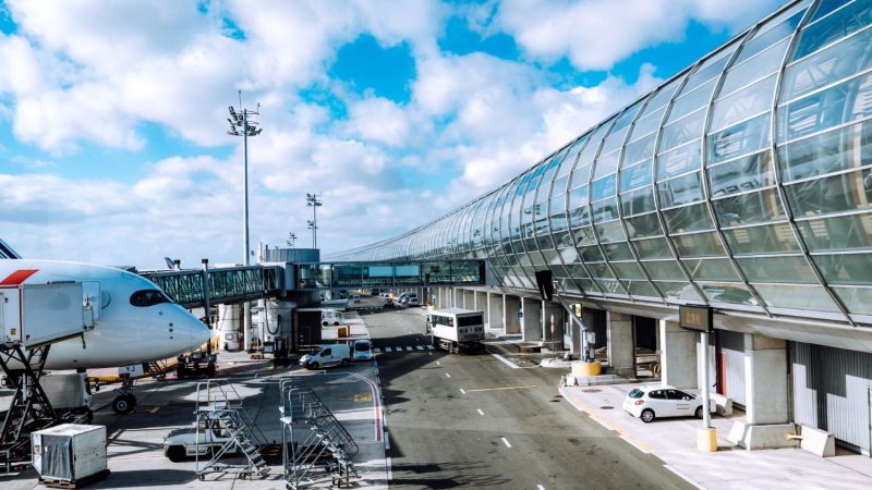 Passasjerområde på en flyplass i Paris med moderne stål- og glassfasade, fly parkert ved gaten og servicekjøretøy på bakken.